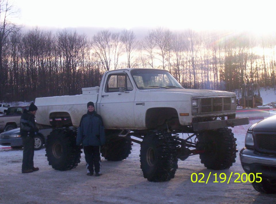 White lifted pickup truck with two people standing next to it in a snowy outdoor setting