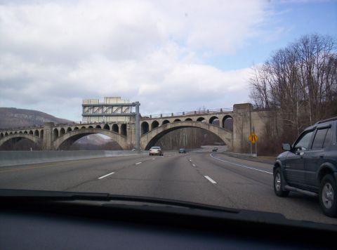 1995 Ford Bronco - A dark SUV drives on a highway under a large concrete bridge with many arches.