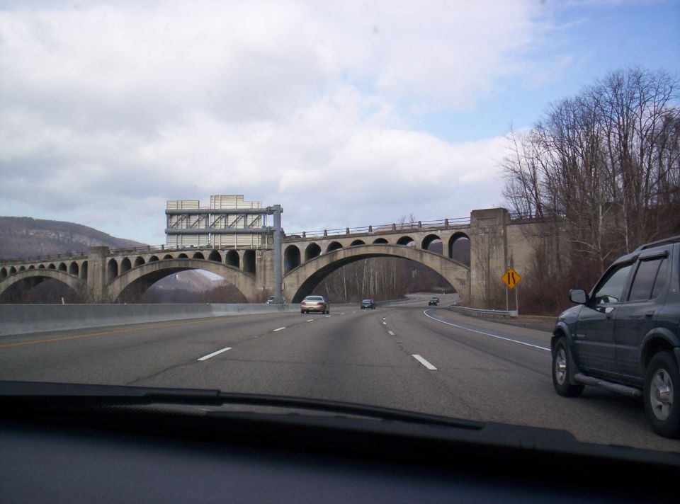 Dark SUV on highway next to a concrete bridge with multiple arches