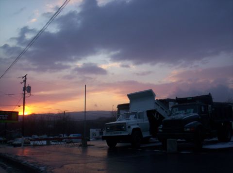 1995 Ford Bronco - Dump trucks are parked on a wet lot during a colorful sunset.