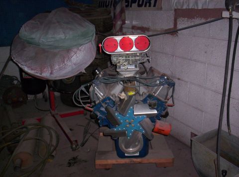 1971 Ford Mustang - V8 engine with a prominent triple carburetor setup and a blue fan is displayed on a stand.