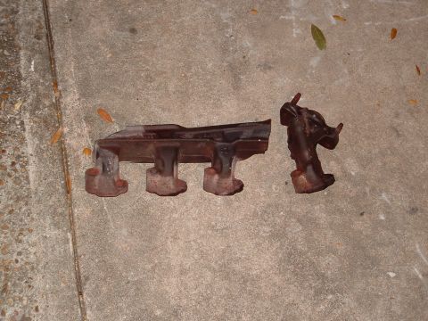 1989 Ford Bronco - These are two separate, rusty exhaust manifold pieces lying on a concrete surface.
