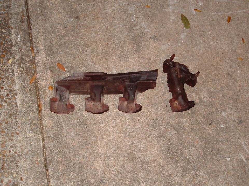 Two rusty exhaust manifold sections on concrete