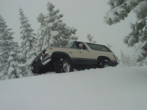 1986 Ford Bronco - A 1980s Ford Bronco navigates a snowy terrain with snow-covered trees in the background.