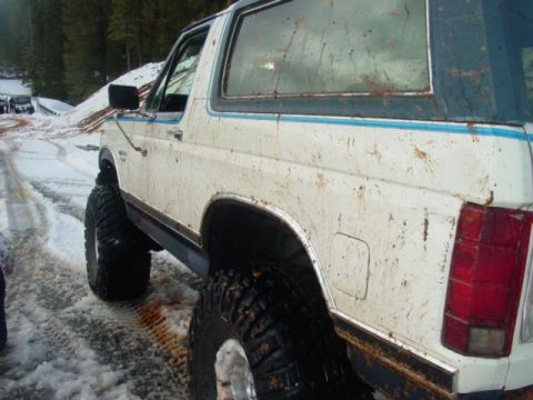 1986 Ford Bronco - 1986 Ford Bronco with large tires driving on a snowy road.