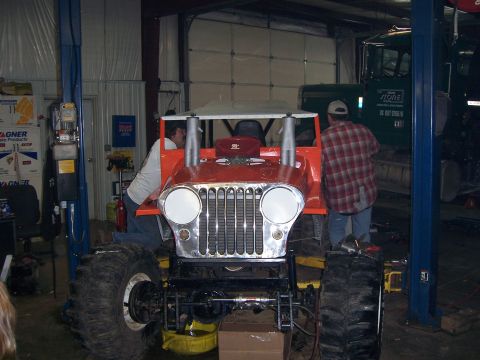 1999 Jeep TJ - This heavily modified Jeep CJ-series is undergoing work in a garage, oversized tires and prominent exhaust pipes.