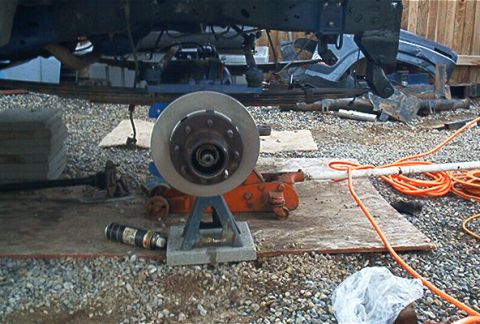 1986 Ford Bronco - A vehicle's undercarriage is supported by jack stands as it undergoes repairs, with brake components exposed.