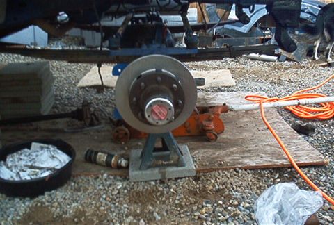 1986 Ford Bronco - A vehicle's brake rotor and hub assembly is supported by a jack stand during maintenance.