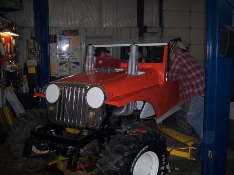 1999 Jeep TJ - Customized 1999 Jeep TJ undergoing modifications in a workshop, large off-road tires and exhaust stacks.