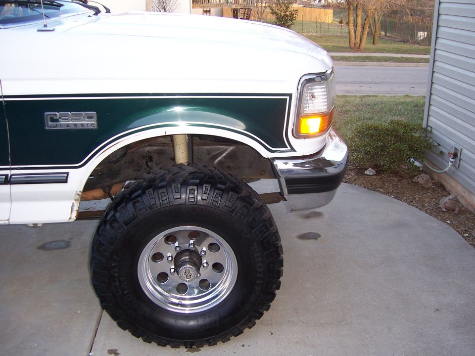 Green and white lifted Ford F350 front wheel with large mud tire on polished rim