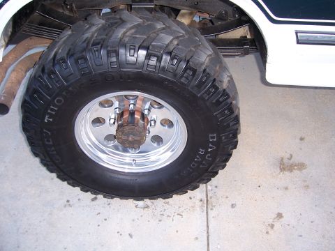 1992 Ford C-250 (Centurion Conversions) - A close-up shot focuses on the massive tire and wheel assembly of a lifted vehicle, showing suspension and exhaust components.