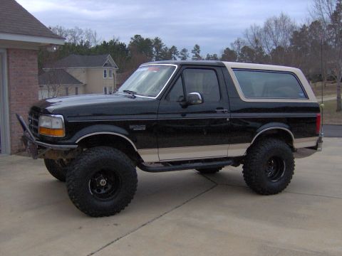 1993 Ford Bronco - This lifted Ford Bronco has a custom bumper and side steps, parked in front of a brick garage.