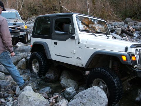 1980 Ford Bronco - A white Jeep Wrangler carefully maneuvers through a rocky stream, with a blue Ford Bronco following behind.