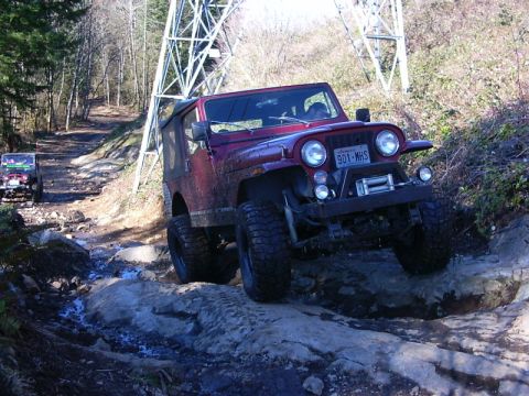 1990 Ford Bronco - Two off-road vehicles navigate a challenging rocky path near a power line tower.