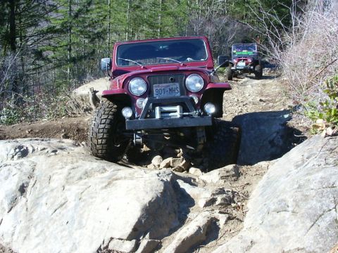 1990 Ford Bronco - A red Jeep CJ-7 navigates a rocky off-road path, with another Jeep visible in the background.