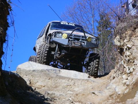 1990 Ford Bronco - Modified SUV navigates a challenging rock obstacle on a trail. The vehicle appears to be from the late 1980s or early 1990s.