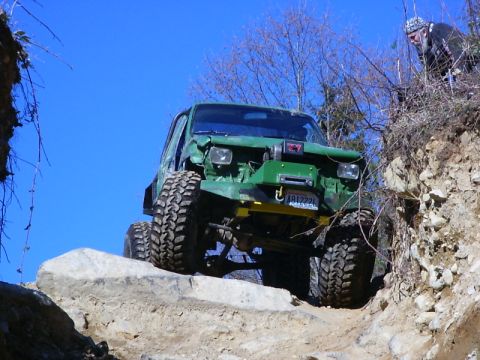 1990 Ford Bronco - This heavily modified SUV navigates a challenging rocky terrain under a clear blue sky.