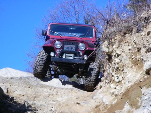 1990 Ford Bronco - This off-road vehicle navigates a challenging rocky path under a clear blue sky.