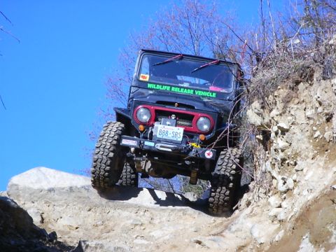 1990 Ford Bronco - Off-road vehicle navigating a challenging rocky terrain under a clear blue sky.