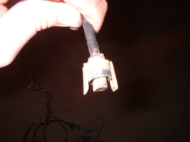 Hand holding a white electrical connector with a black wire attached. Loose wires are visible below