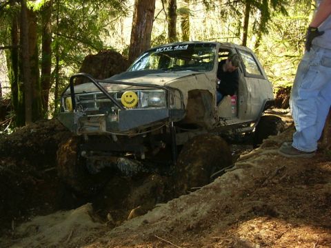 1990 Ford Bronco - This heavily modified off-road vehicle appears to be stuck deep in the mud while navigating a wooded trail.