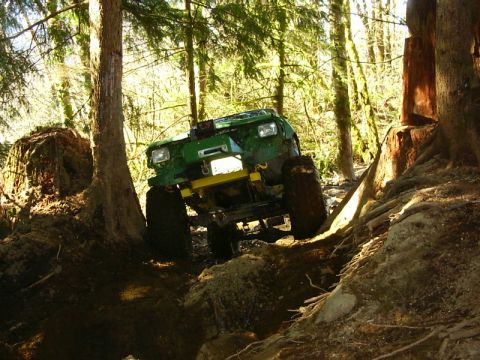1990 Ford Bronco - A modified off-road vehicle tackles a challenging, uneven terrain in a forest setting.