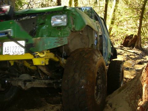 1990 Ford Bronco - A heavily modified green off-road vehicle navigates a muddy trail in a wooded area.