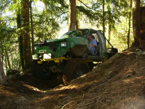 1990 Ford Bronco - This heavily modified off-road vehicle navigates a challenging wooded terrain with a visible roll cage.
