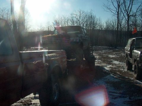 1995 Ford Bronco - Multiple trucks are parked in a muddy, outdoor area under a bright, sunny sky.