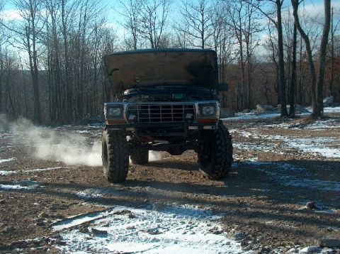 1995 Ford Bronco - This heavily modified 1980 Ford Bronco is shown from the front with its hood raised, kicking up dust in a wooded area.