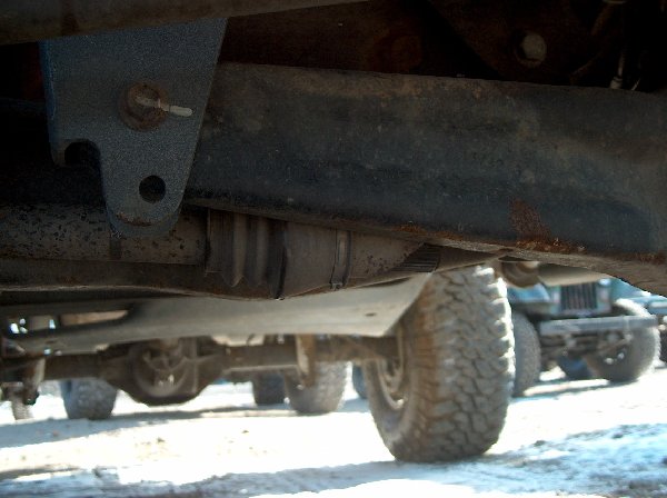 Undercarriage view of a vehicle with off-road tires and other vehicles in the background