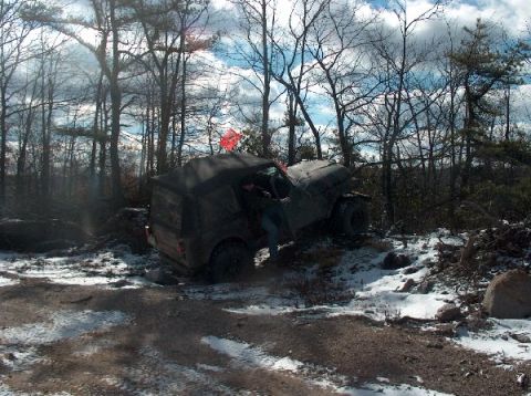 1995 Ford Bronco - A person exits an off-road vehicle that appears stuck in a wooded area with patches of snow on the ground.