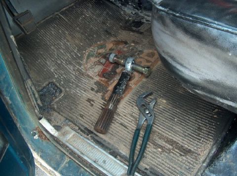 1995 Ford Bronco - A steering linkage part and pliers are on the worn floor mat inside a vehicle.