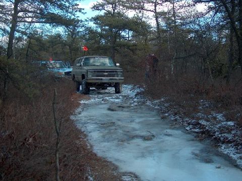 1995 Ford Bronco - Two SUVs navigate a muddy and icy path through a wooded area.