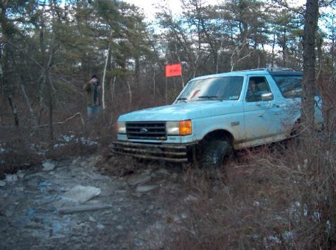 1995 Ford Bronco - A light blue 1987 Ford Bronco navigates a muddy, wooded trail.