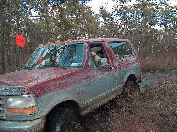 Red and grey 1995 Ford Bronco driving through mud, driver visible