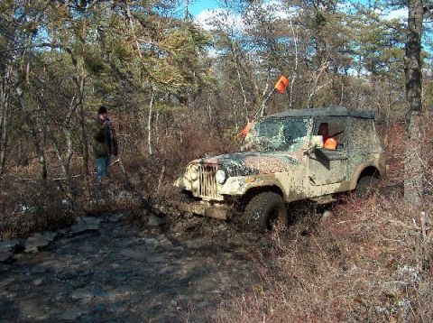 1995 Ford Bronco - Jeep CJ-7 navigating a muddy off-road course in a wooded area.