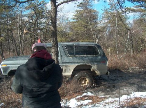 1995 Ford Bronco - A gray Ford Bronco is stuck in the mud in a wooded area, with snow on the ground.