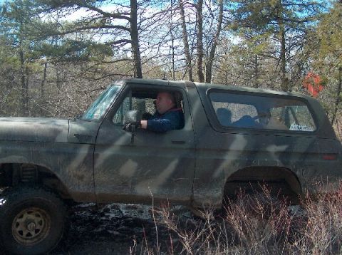 1995 Ford Bronco - A man drives a camouflage Ford Bronco through a wooded area with dry brush.