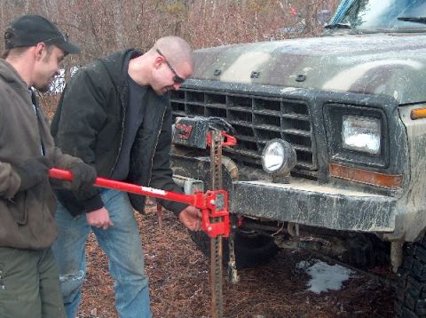 1995 Ford Bronco - Two men operate a red hi-lift jack attached to the front bumper of a camouflage Ford truck.