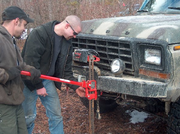Red hi-lift jack attached to front bumper of a camouflage Ford truck