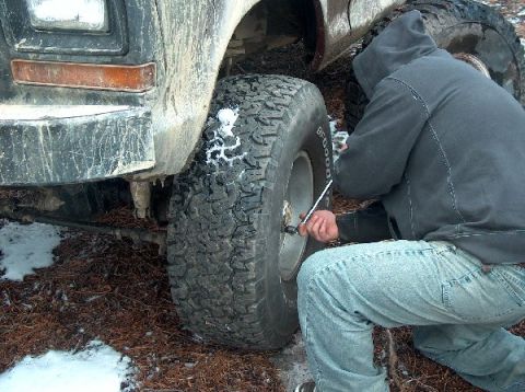 1995 Ford Bronco - A person is shown changing a tire on a vehicle in a wooded area with some snow on the ground.