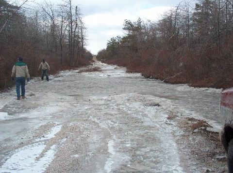 1995 Ford Bronco - A portion of a red vehicle is visible on the right side of an icy road, with two people walking ahead.