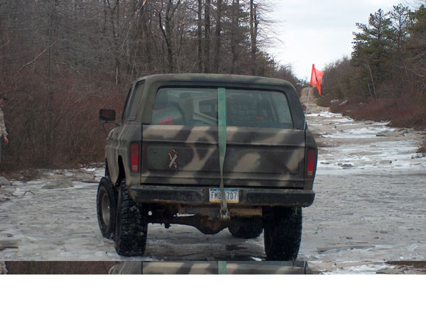 Rear view of a camouflaged SUV with lifted suspension on an icy, wooded road. License plate reads FMB 707