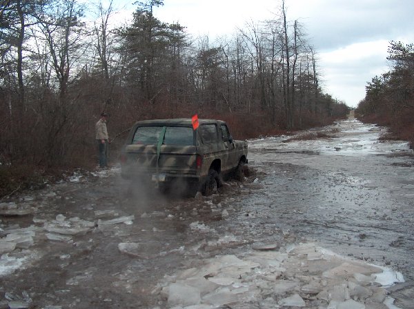 Camouflaged SUV stuck in icy mud on a dirt road, person standing nearby
