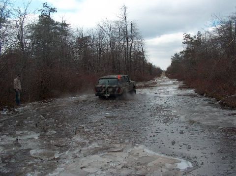 1995 Ford Bronco - A camouflaged Ford Bronco navigates a treacherous icy and muddy path in a wooded landscape.