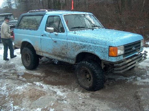 1995 Ford Bronco - A light blue 1987 Ford Bronco is covered in mud and driving through a snowy, wet terrain.