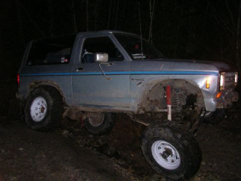 1984 Ford Bronco II - A lifted 1984 Ford Bronco II is shown on a muddy trail in a wooded area at night.