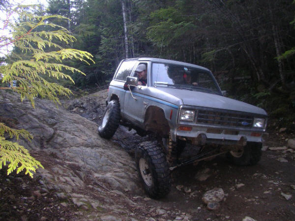 Silver 1984 Ford Bronco II off-roading on a rocky trail, front 3/4 view
