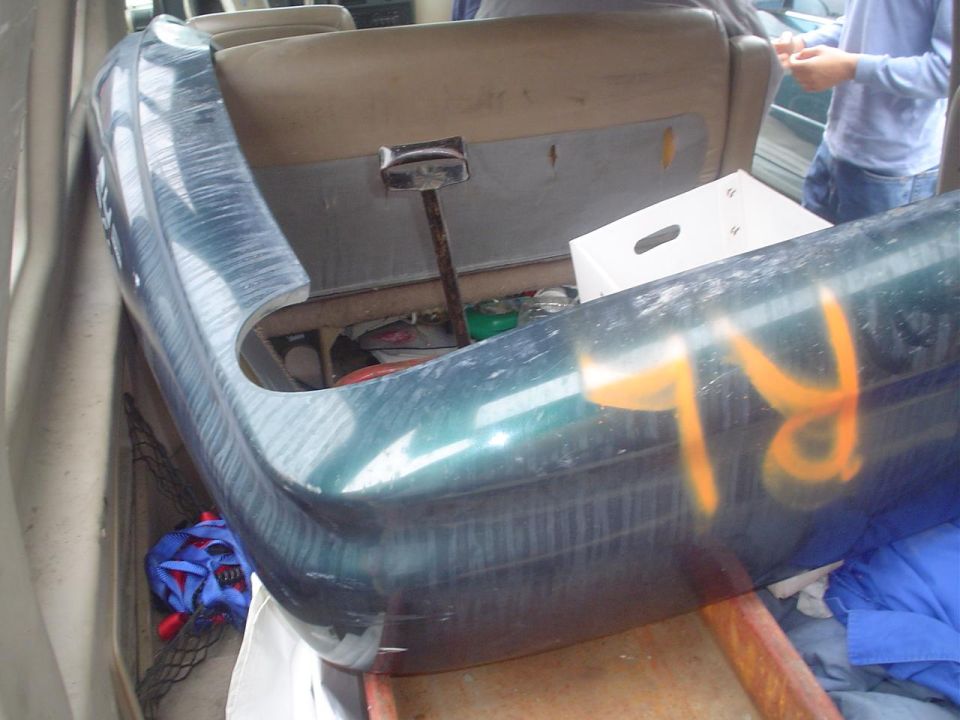Green car bumper with orange markings inside a vehicle, near seats and a white box
